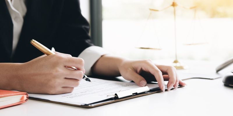 Business woman and lawyers discussing contract papers with brass scale on wooden desk in office. Law